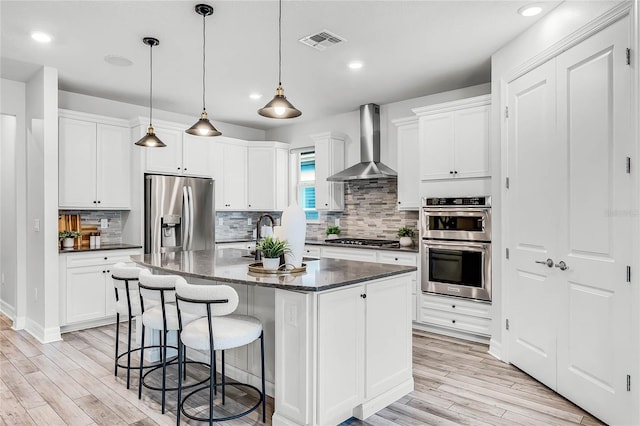 kitchen with visible vents, a breakfast bar, light wood-style flooring, stainless steel appliances, and wall chimney exhaust hood