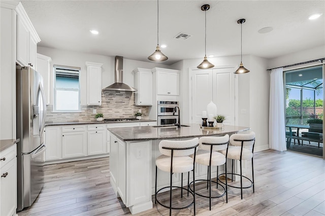 kitchen with visible vents, a kitchen breakfast bar, tasteful backsplash, stainless steel appliances, and wall chimney range hood