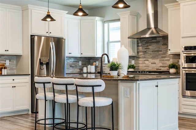 kitchen featuring backsplash, wall chimney range hood, a breakfast bar, appliances with stainless steel finishes, and light wood-style floors