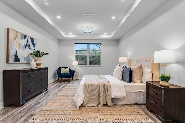 bedroom with a tray ceiling, baseboards, visible vents, and light wood finished floors