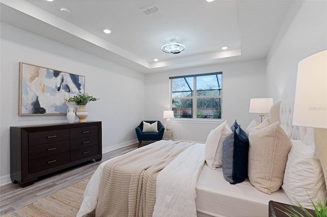 bedroom with baseboards, visible vents, light wood finished floors, recessed lighting, and a raised ceiling