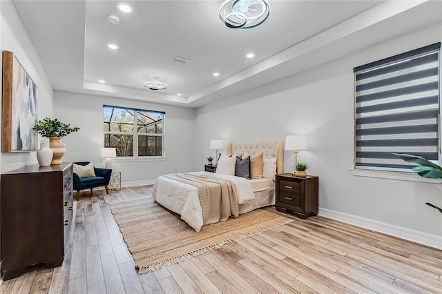 bedroom with baseboards, visible vents, a tray ceiling, recessed lighting, and light wood-style floors