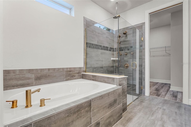 bathroom featuring baseboards, wood tiled floor, a shower stall, a spacious closet, and a bath