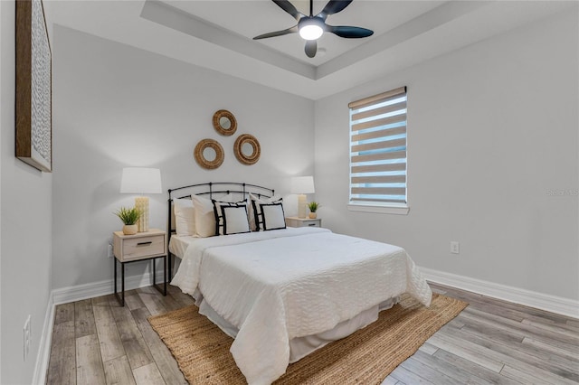 bedroom featuring a ceiling fan, a raised ceiling, baseboards, and wood finished floors