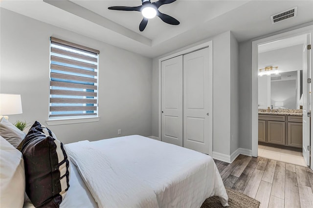 bedroom with visible vents, connected bathroom, light wood-style floors, a closet, and a ceiling fan