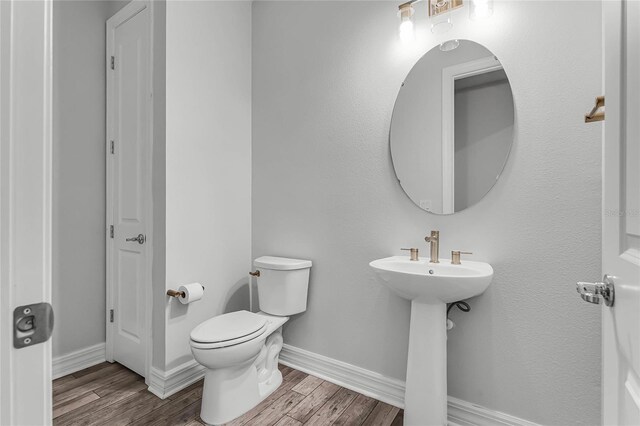 half bathroom with a sink, toilet, baseboards, and wood finished floors