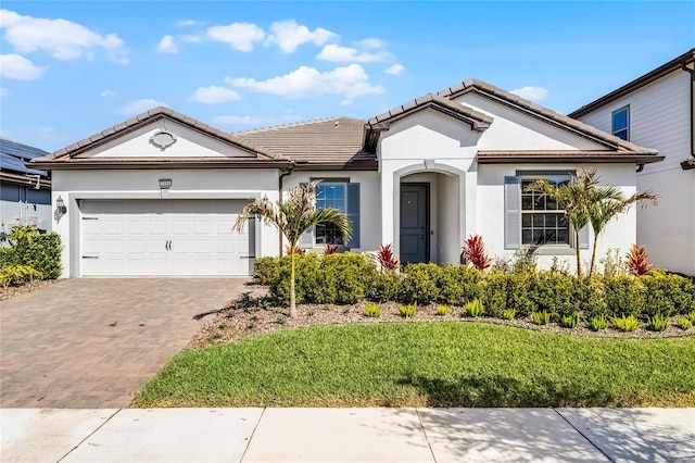 view of front of property featuring a tile roof, a front yard, stucco siding, decorative driveway, and an attached garage