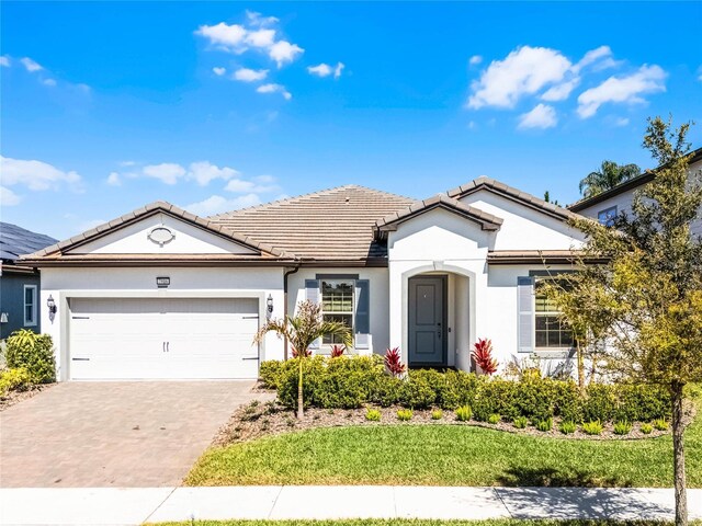 ranch-style home featuring stucco siding, a tile roof, decorative driveway, a front yard, and a garage