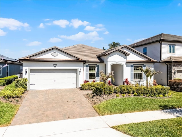 view of front of home with decorative driveway, a tiled roof, an attached garage, and stucco siding