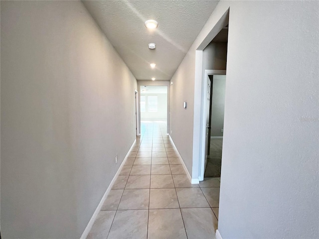 hall featuring baseboards, a textured ceiling, and light tile patterned flooring