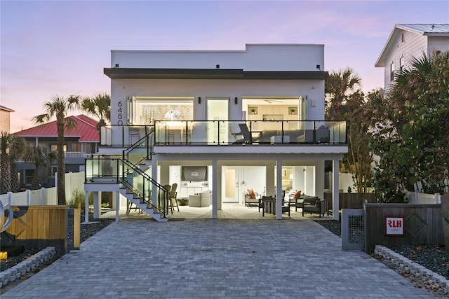 back of property at dusk featuring fence, a patio, a balcony, and stucco siding