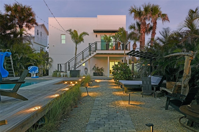 rear view of house with stairs, stucco siding, an outdoor pool, outdoor dining space, and a patio area