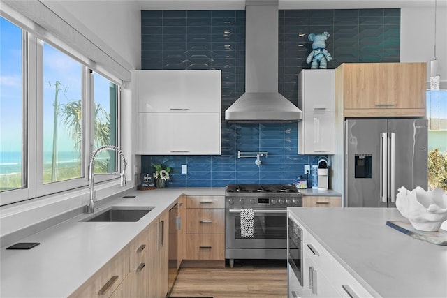 kitchen with light countertops, appliances with stainless steel finishes, a sink, modern cabinets, and wall chimney exhaust hood