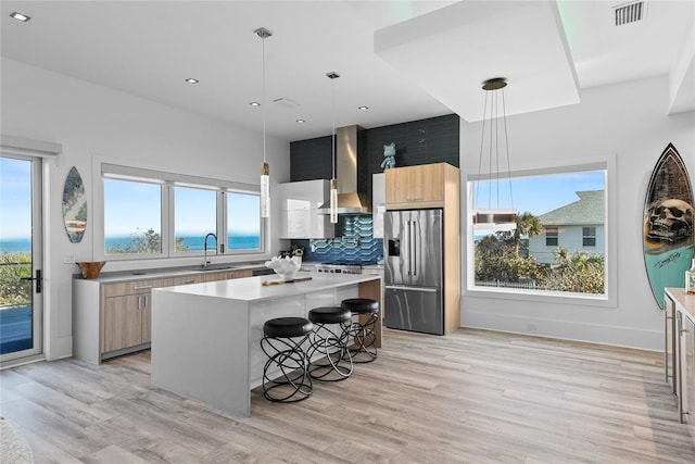 kitchen with a sink, visible vents, high end fridge, wall chimney exhaust hood, and modern cabinets