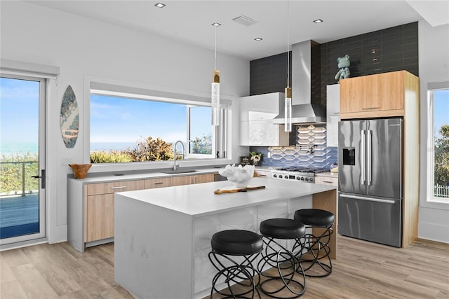 kitchen with light countertops, a sink, modern cabinets, stainless steel fridge, and wall chimney exhaust hood