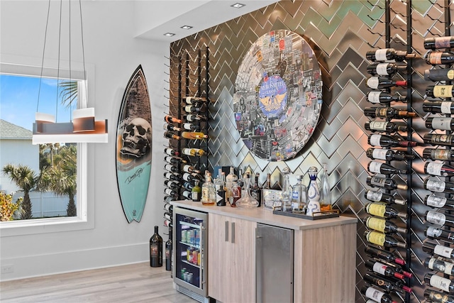 wine room with light wood-type flooring, beverage cooler, and a wealth of natural light