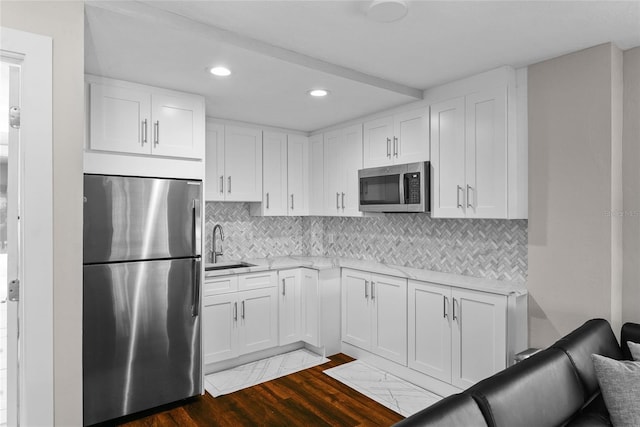 kitchen featuring light countertops, backsplash, appliances with stainless steel finishes, dark wood-type flooring, and a sink