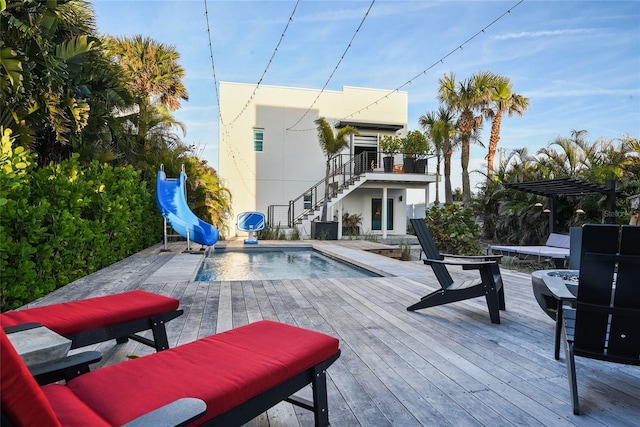 pool with a water slide, stairway, and a wooden deck