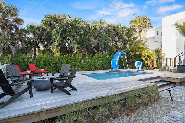 pool featuring a fire pit, a deck, and a water slide