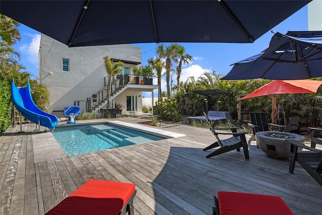 pool featuring a deck, an outdoor fire pit, a water slide, and stairway