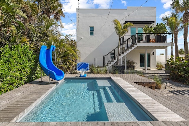 rear view of house featuring a deck, stairway, an outdoor pool, and stucco siding