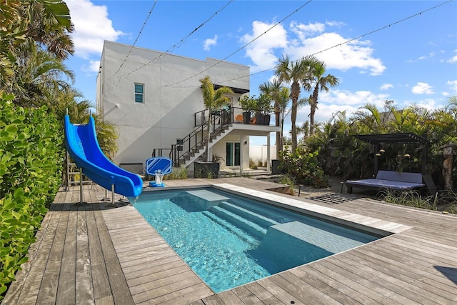 pool featuring stairway, a water slide, and a wooden deck