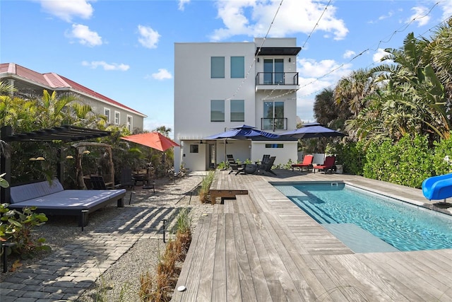 rear view of property with a balcony, outdoor dining area, an outdoor pool, and stucco siding