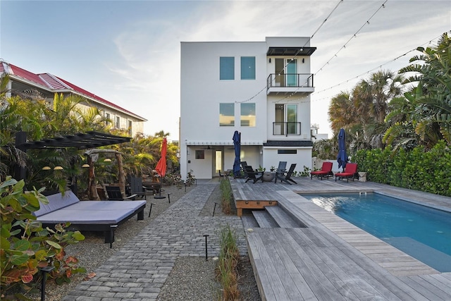 rear view of property with an outdoor pool, a balcony, a deck, a pergola, and stucco siding