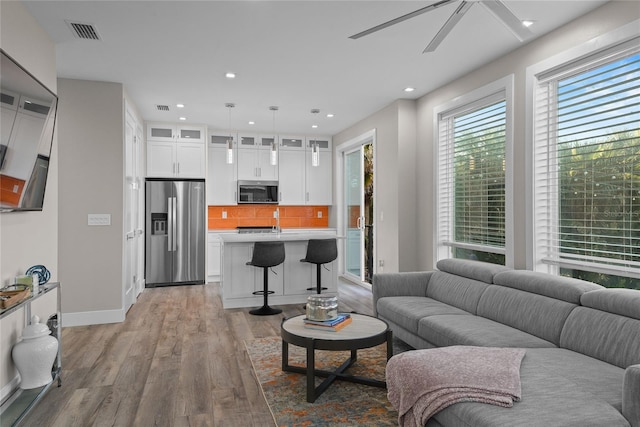 living area with recessed lighting, visible vents, ceiling fan, light wood-type flooring, and baseboards