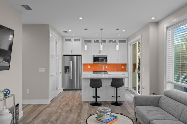 kitchen featuring light wood finished floors, stainless steel appliances, light countertops, visible vents, and open floor plan