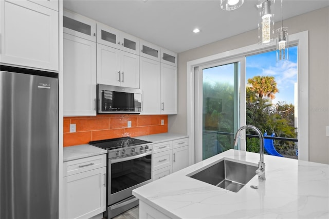 kitchen with light stone counters, appliances with stainless steel finishes, decorative backsplash, and a sink