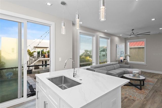 kitchen with wood finished floors, a sink, open floor plan, light stone countertops, and decorative light fixtures