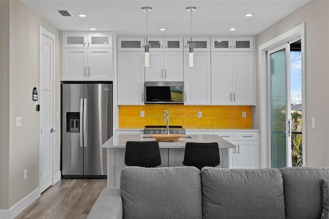 kitchen featuring visible vents, open floor plan, light countertops, appliances with stainless steel finishes, and a center island with sink