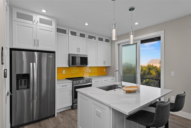 kitchen featuring tasteful backsplash, dark wood-style floors, a kitchen island with sink, stainless steel appliances, and a sink