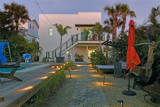 rear view of house with a patio area, stairs, an outdoor pool, and stucco siding