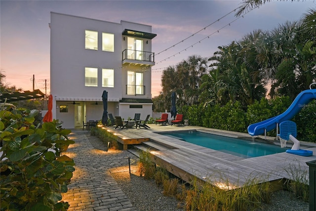 back of property with a balcony, a patio area, an outdoor pool, and stucco siding