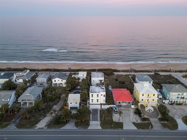 aerial view at dusk with a view of the beach, a water view, and a residential view