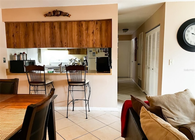 kitchen featuring a peninsula, light tile patterned floors, stainless steel microwave, and freestanding refrigerator