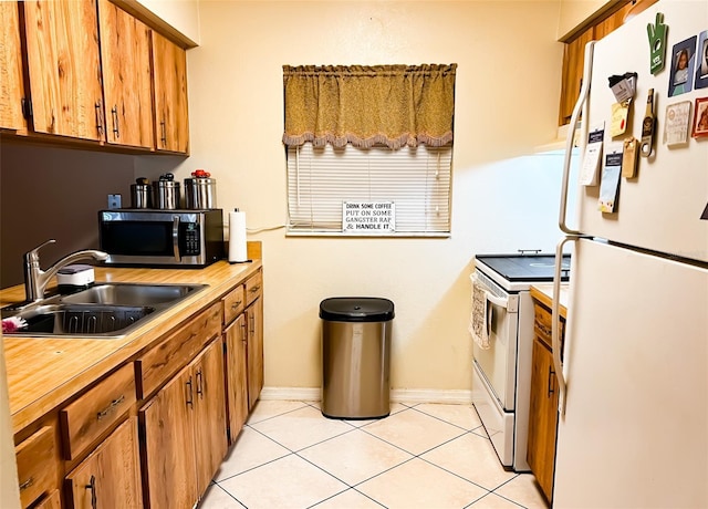 kitchen with brown cabinets, light tile patterned flooring, a sink, white appliances, and baseboards