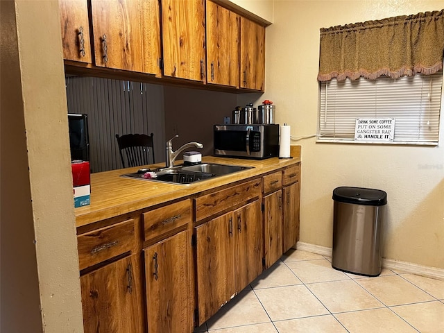 kitchen with brown cabinetry, stainless steel microwave, light countertops, a sink, and light tile patterned flooring