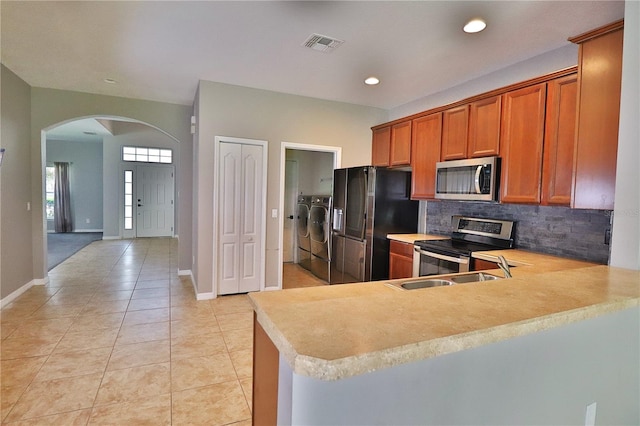 1862 Great Falls Way, Orlando, FL 32824 - kitchen with appliances with stainless steel finishes, washing machine and dryer, arched walkways, brown cabinets, and light tile patterned flooring