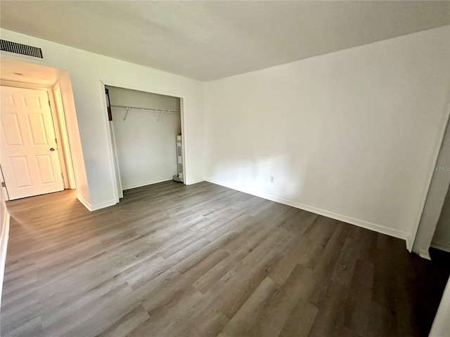 unfurnished bedroom with dark wood-type flooring, baseboards, visible vents, and a closet