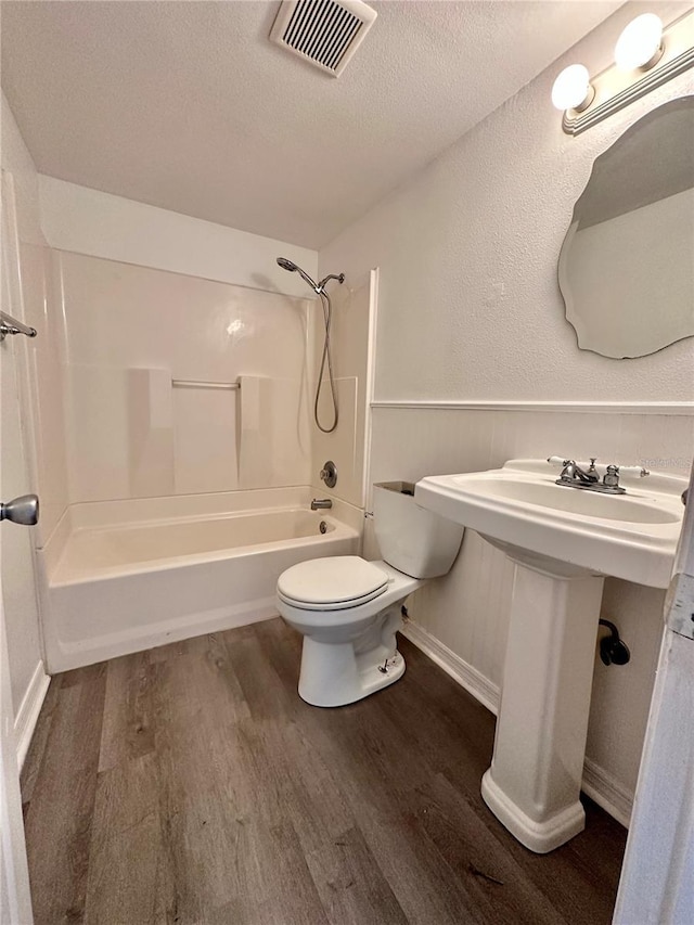 full bath with visible vents, toilet, a textured ceiling, wood finished floors, and bathing tub / shower combination