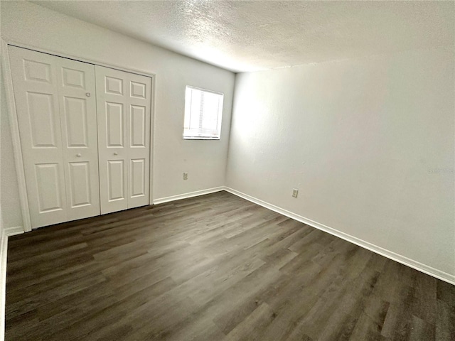 unfurnished bedroom with a closet, baseboards, a textured ceiling, and dark wood-style floors