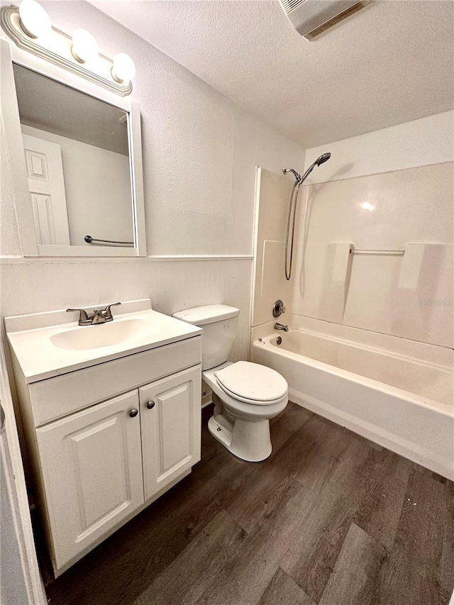 bathroom featuring toilet, a textured ceiling, wood finished floors, tub / shower combination, and vanity