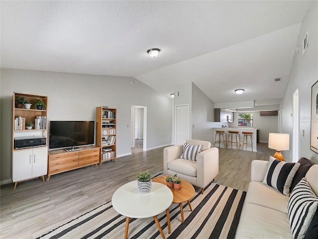 living area with lofted ceiling, visible vents, a textured ceiling, and light wood finished floors