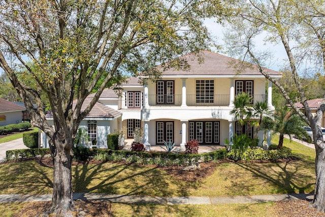 view of front of property featuring a balcony, stucco siding, a front lawn, and french doors