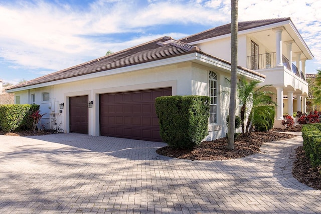 view of side of property with decorative driveway, a balcony, an attached garage, and stucco siding