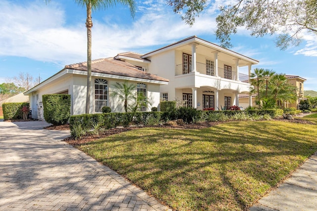 view of front of home featuring a balcony, a garage, decorative driveway, stucco siding, and a front yard