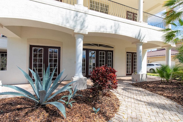 view of exterior entry featuring french doors, a balcony, and stucco siding